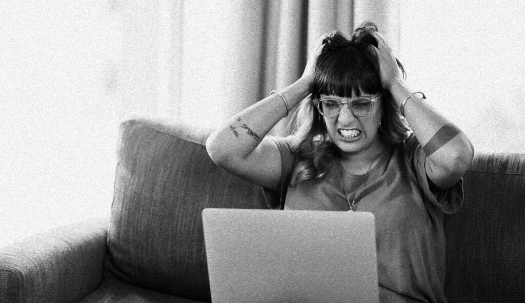 A business owner frustratedly reviewing business marketing strategies on a laptop, surrounded by notes and planning materials, representing clarity and focus in attracting ideal clients.
